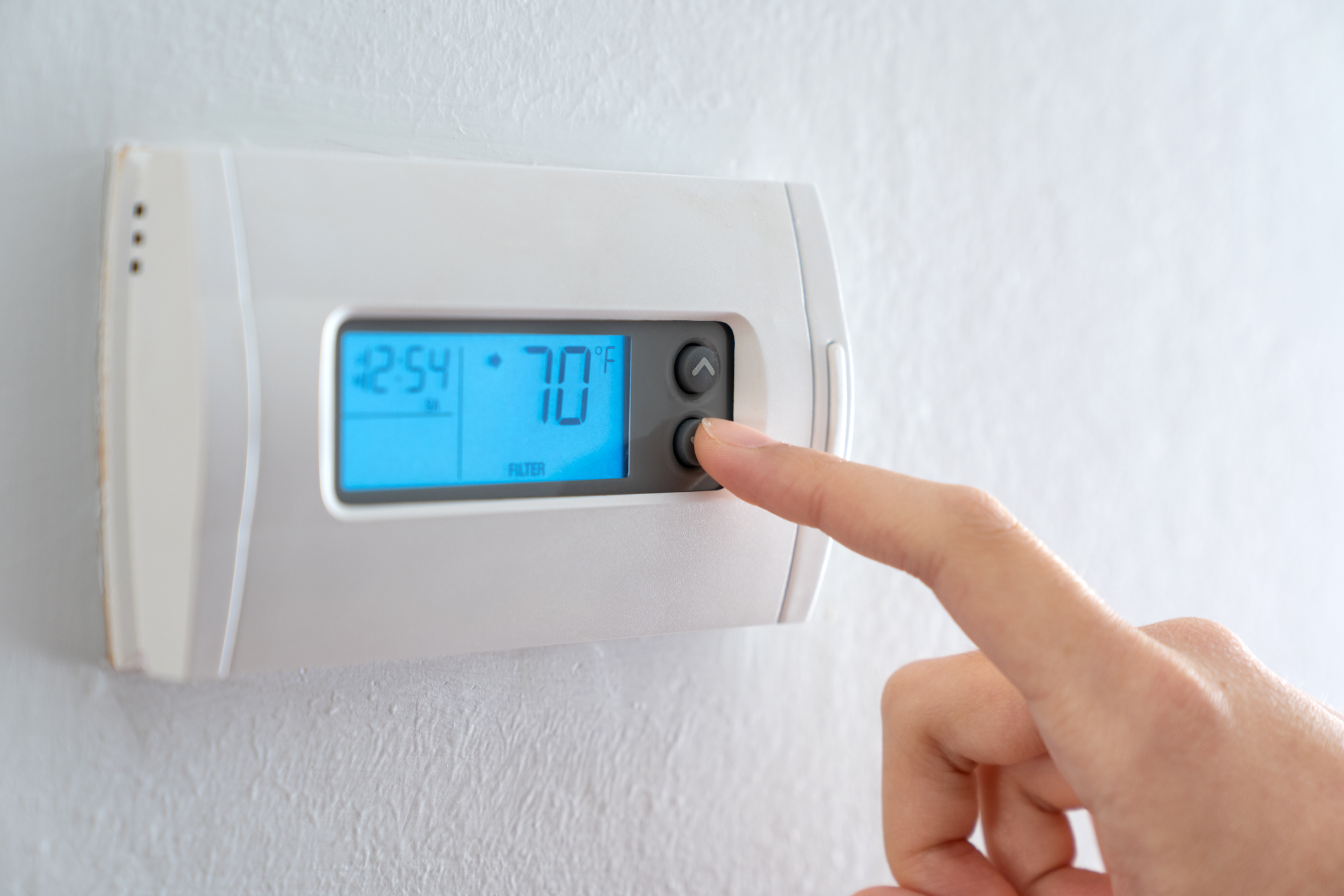 A woman is pressing the down button of a wall attached house thermostat